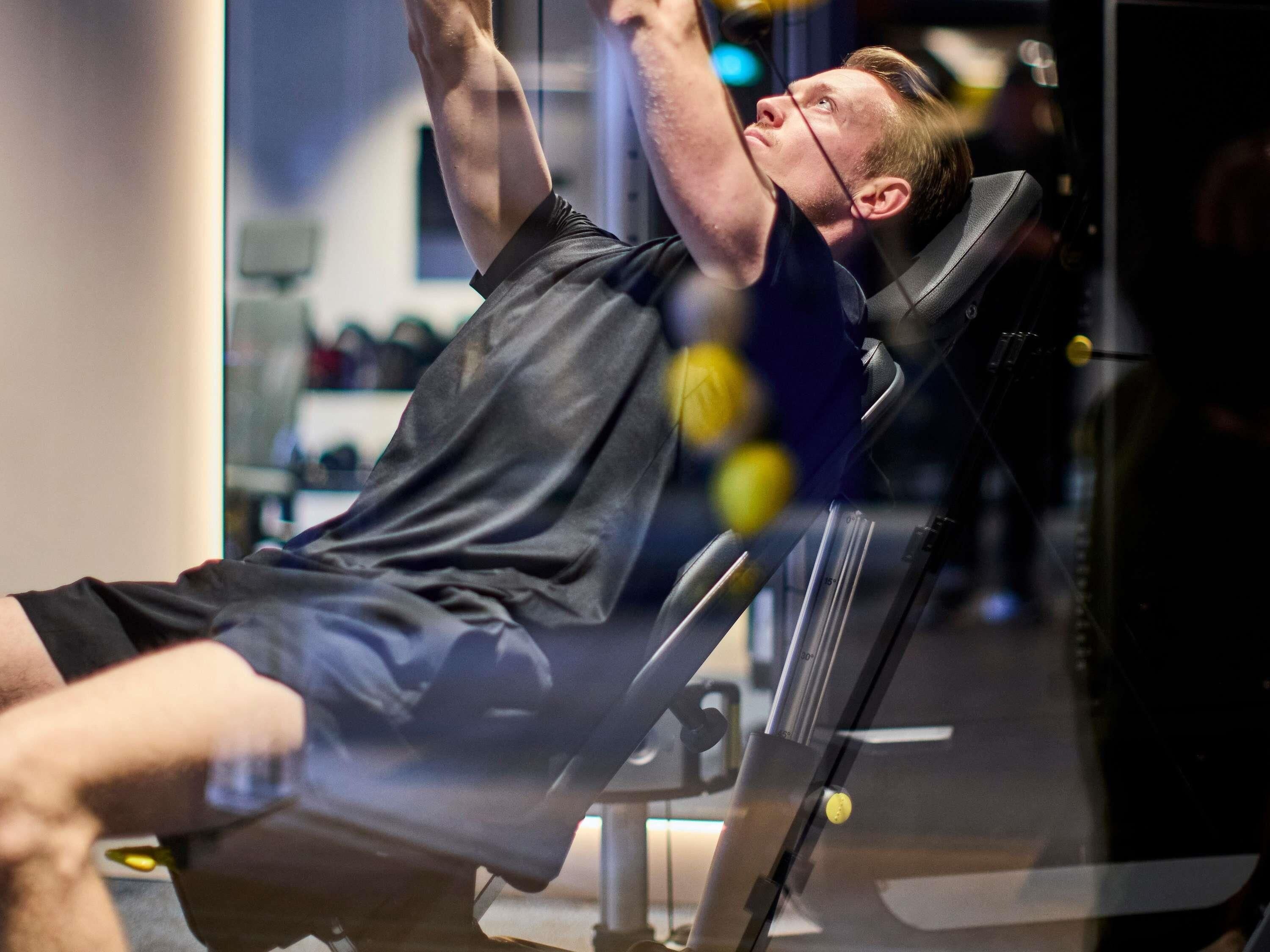 Une personne utilise un appareil d’aviron dans une salle de sport, avec d’autres équipements d’exercice en arrière-plan.