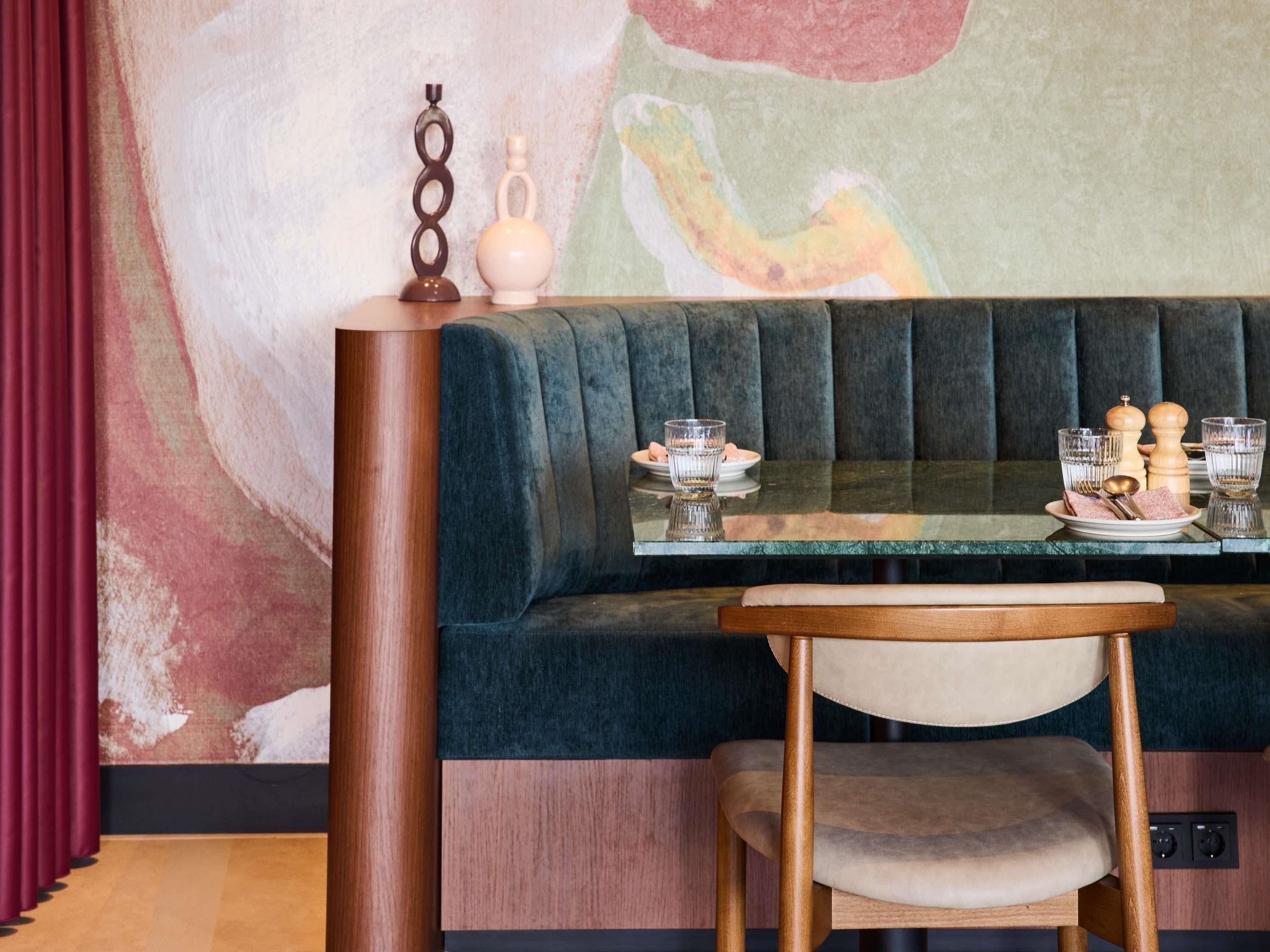 A seating area with a cushioned bench, a table with a glass top, and a wall with abstract art.