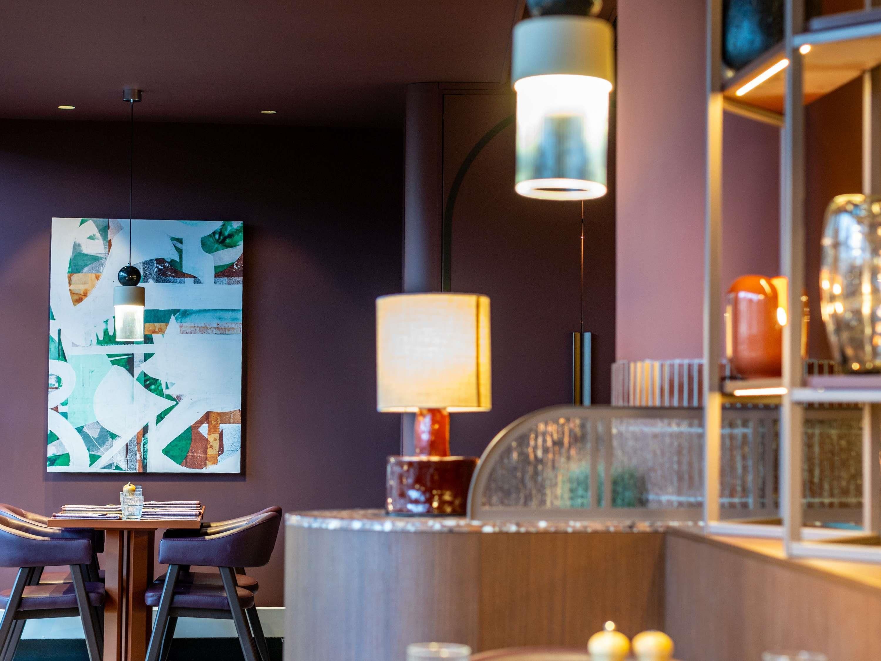 Un comedor con una mesa, sillas, una lámpara y una pared decorada con arte abstracto.