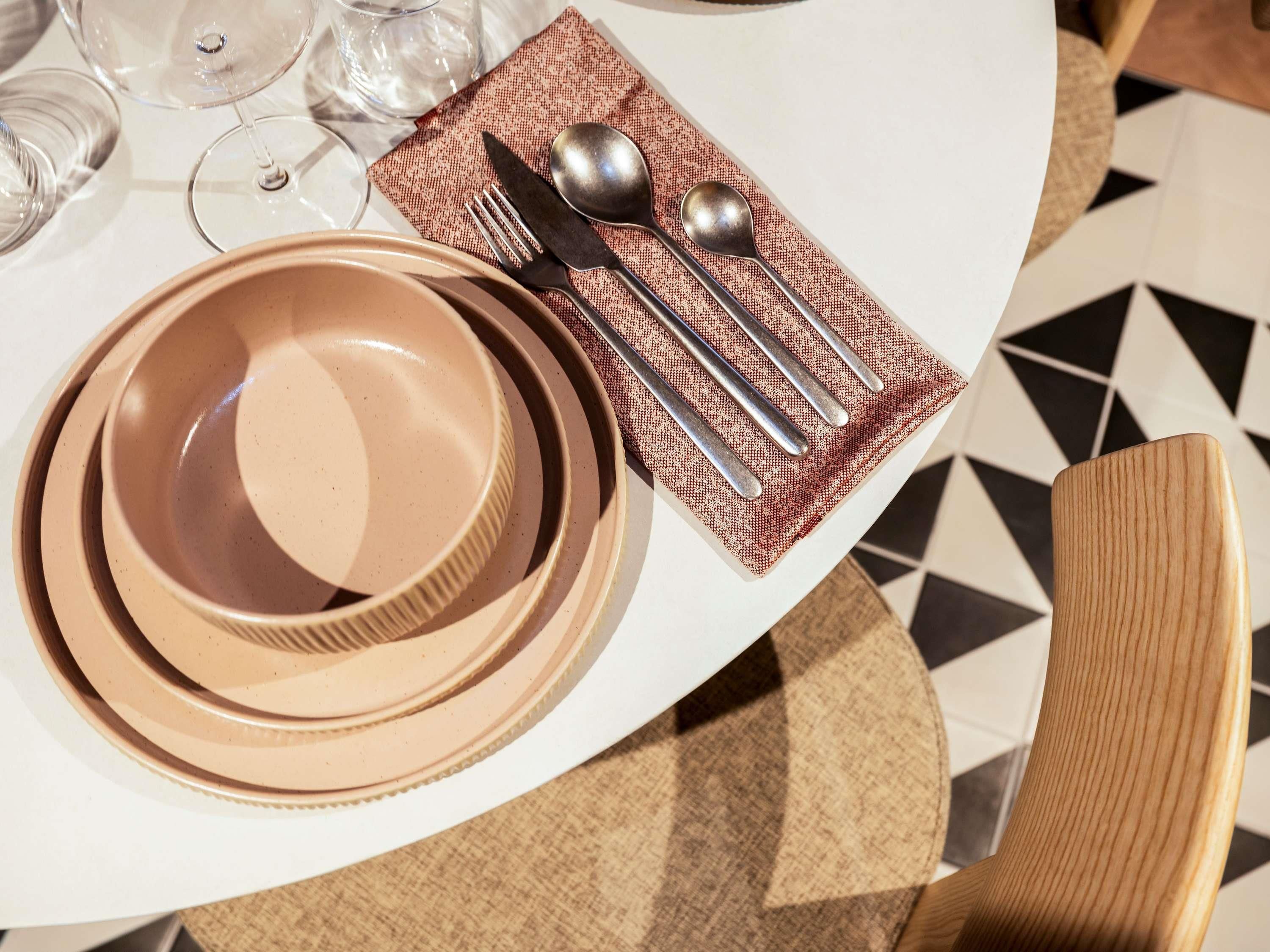 A table set with plates, cutlery, and glasses, with a patterned napkin and a wooden chair.