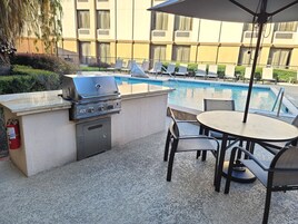 Um pátio externo com churrasqueira, área de estar e piscina.