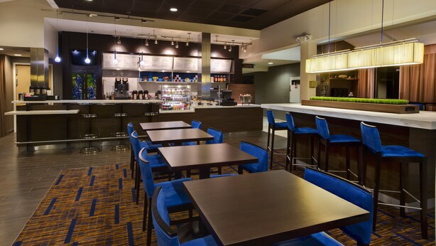 A modern restaurant with a bar area, seating with blue chairs, and a patterned carpet. - Heritage Place Houston Brookhollow (Houston)