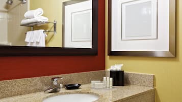 A bathroom with a granite countertop sink, a mirror, a towel rack, and a shower area.