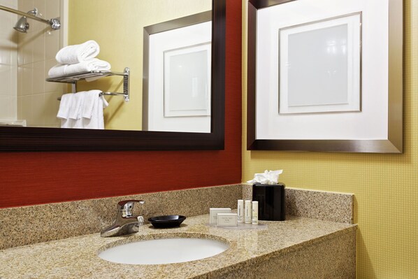 A bathroom with a granite countertop sink, a mirror, a towel rack, and a shower area.
