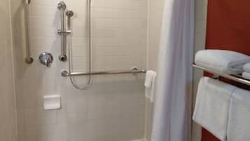 A shower with a handheld showerhead, a handheld shower attachment, and a wall-mounted showerhead. There is a towel rack with two towels and a white shower curtain.