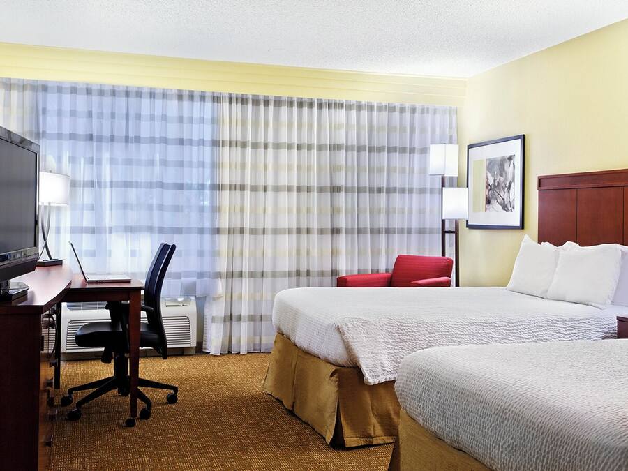 Una habitación de hotel con una cama, un escritorio con computadora, televisor y una silla roja.