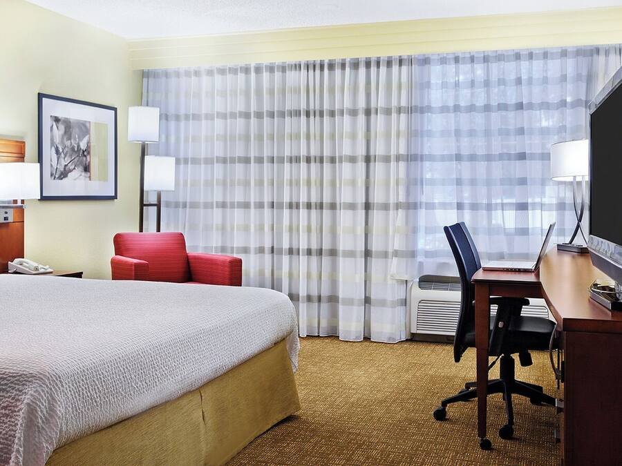 A hotel room with a large bed, a desk with a computer, a chair, a TV, and a window with curtains.