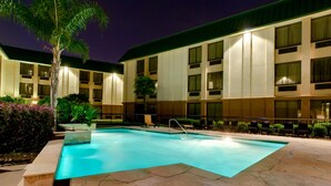 A swimming pool with a stone deck, surrounded by a building with multiple windows and a palm tree. - Heritage Place Houston Brookhollow (Houston)