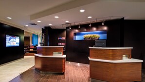 A reception area with wooden reception desks, a large flat-screen TV, and a potted plant. - Heritage Place Houston Brookhollow (Houston)