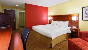 A hotel room with a large bed, a desk, a television, and a red accent wall. - Heritage Place Houston Brookhollow (Houston)