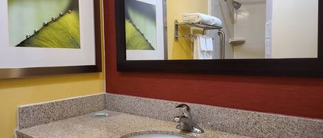 A bathroom with a granite countertop sink, a framed picture, and a mirror reflecting a shower area.
