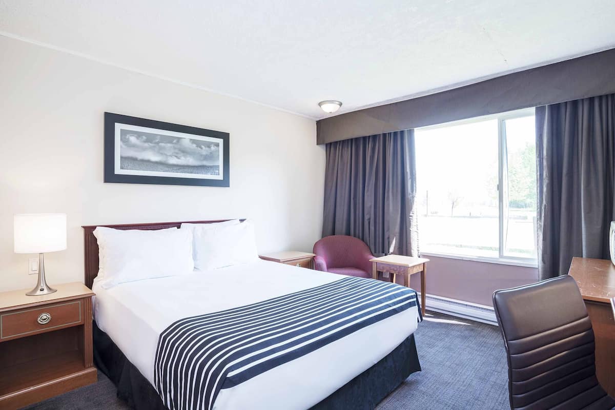 A hotel room with a large bed, a desk, a chair, a lamp, and a window with curtains.