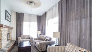 A hotel room with a fireplace, striped sofas, a coffee table, and curtains. - Sandman Inn McBride (McBride)