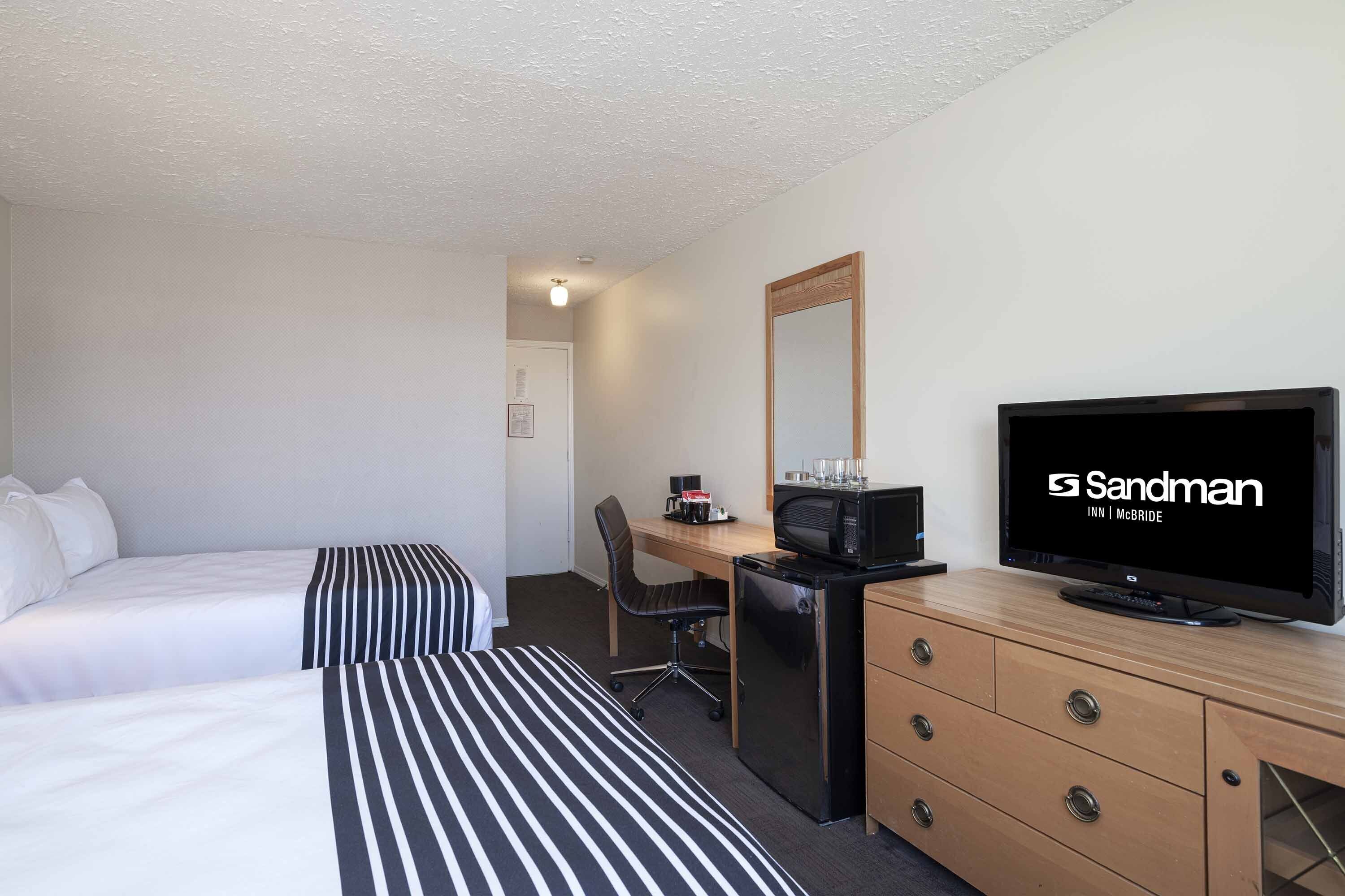 A hotel room with two beds, a desk with a computer, a television, and a refrigerator.