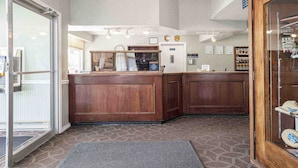 A reception area with a wooden counter, a clock, and a door leading to a room. - Sandman Inn McBride (McBride)
