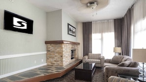 A living room with a stone fireplace, striped armchairs, a sofa, and a coffee table. - Sandman Inn McBride (McBride)
