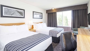 A hotel room with two beds, a desk, a chair, a TV, and two framed pictures on the wall. - Sandman Inn McBride (McBride)