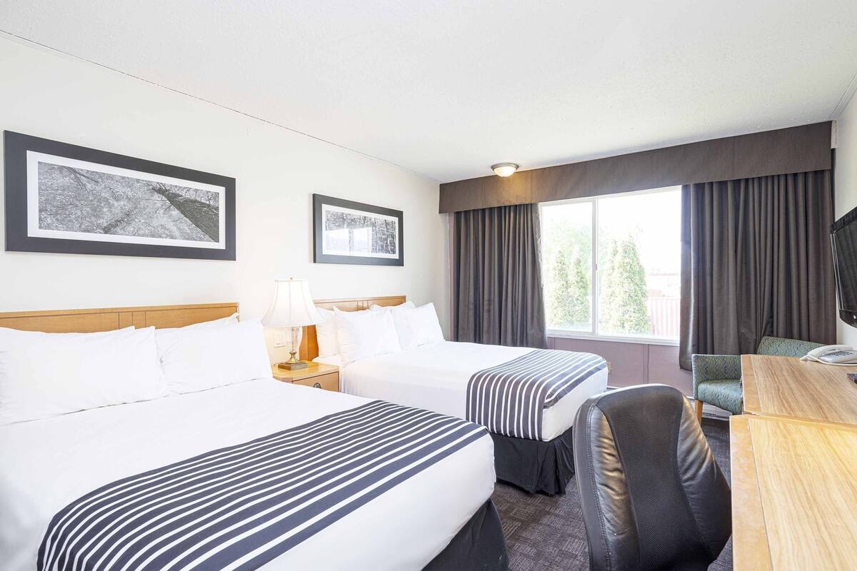A hotel room with two beds, a desk, a chair, a TV, and two framed pictures on the wall.