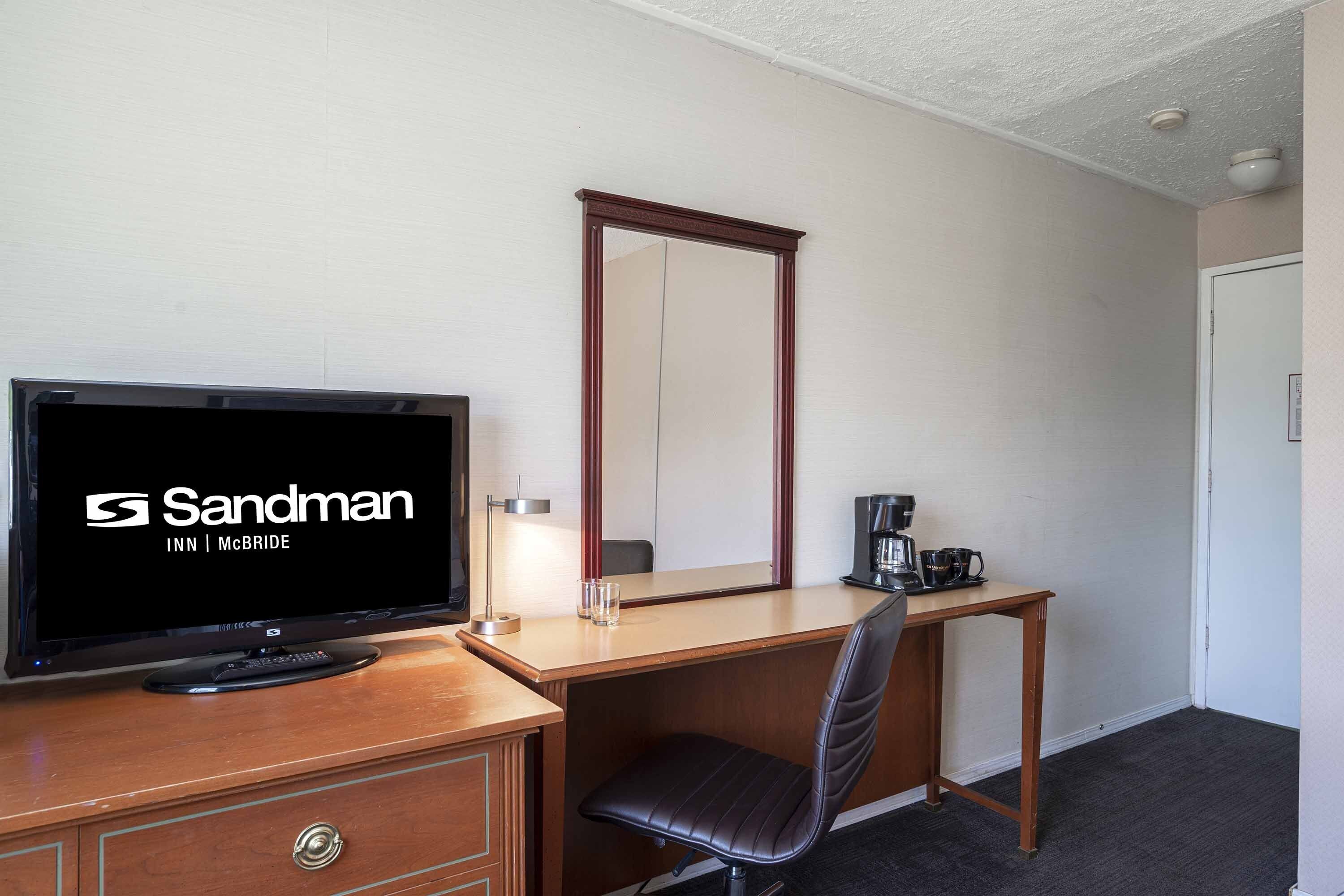A hotel room with a television, a desk, a chair, a coffee maker, and a mirror.