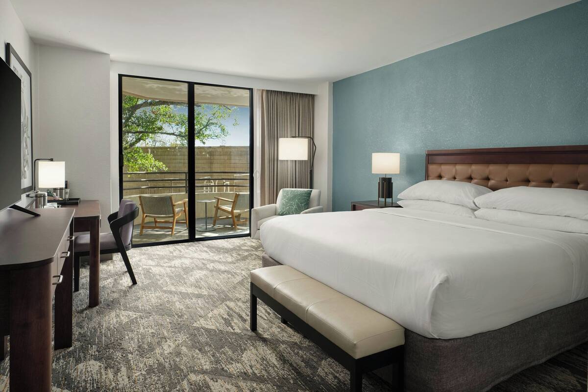 Habitación de hotel con una cama grande, un escritorio, una silla, un banco, una lámpara y vistas al exterior.