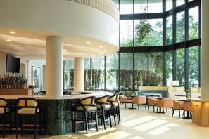 Un espace bar moderne doté d’un comptoir incurvé, de plusieurs tabourets et d’un coin salon avec des tables et des chaises.