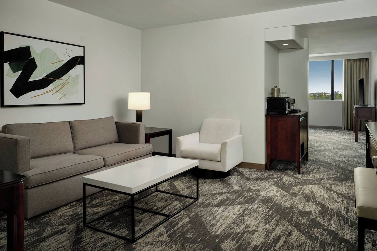 Una habitación de hotel moderna con sofá, sillón, mesa de centro y un cuadro en la pared.
