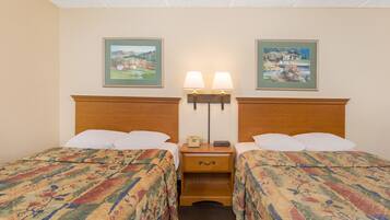 A hotel room with two beds, each with a floral-patterned bedspread, a wooden headboard, a nightstand with a lamp, and two framed pictures on the wall.