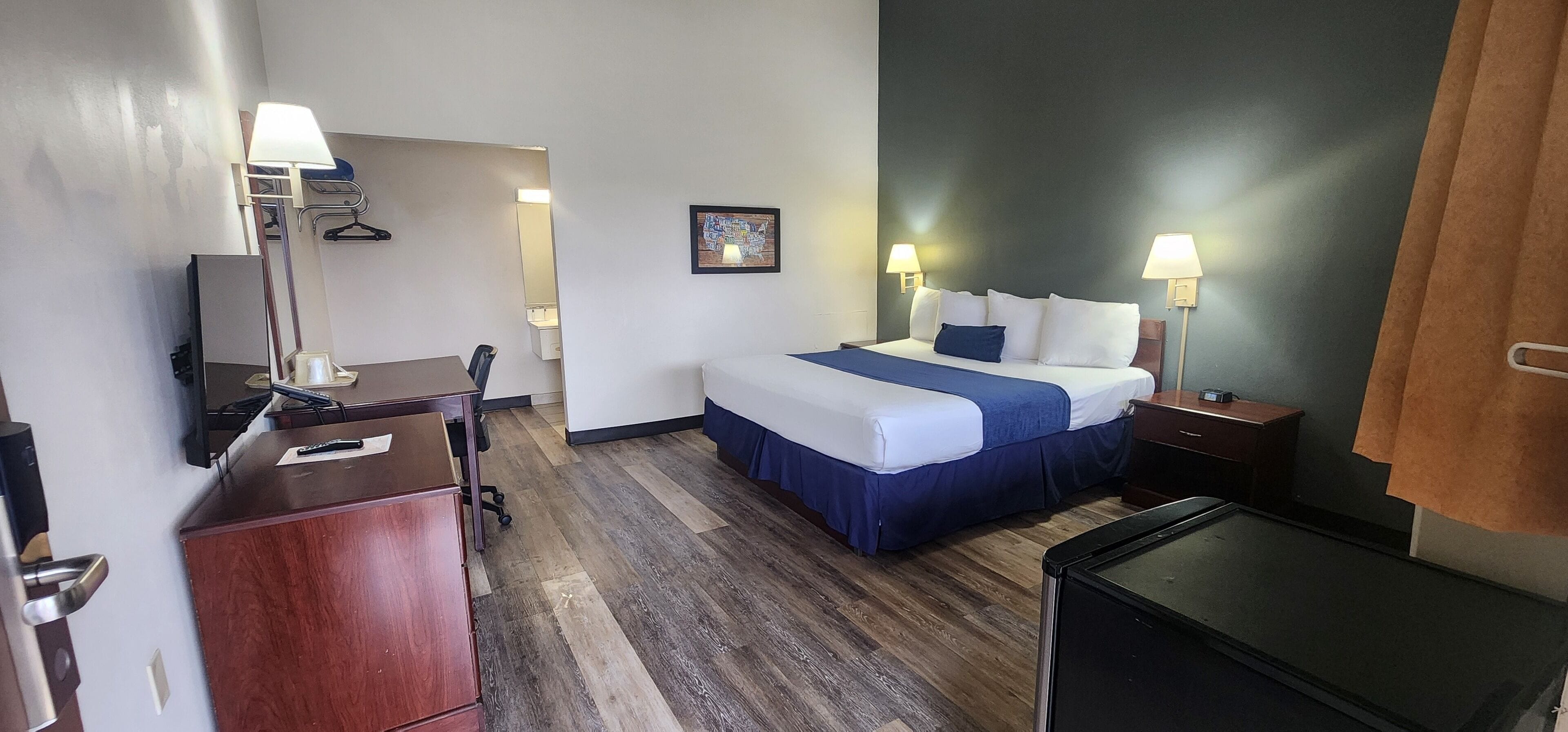 A hotel room with a bed, bedside tables, a desk, a chair, a dresser, and a TV.
