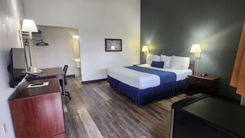 A hotel room with a bed, bedside tables, a desk, a chair, a dresser, and a TV.
