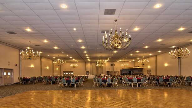 Een ruime congreszaal met rijen tafels en stoelen, kroonluchters en een gepolijste houten vloer.