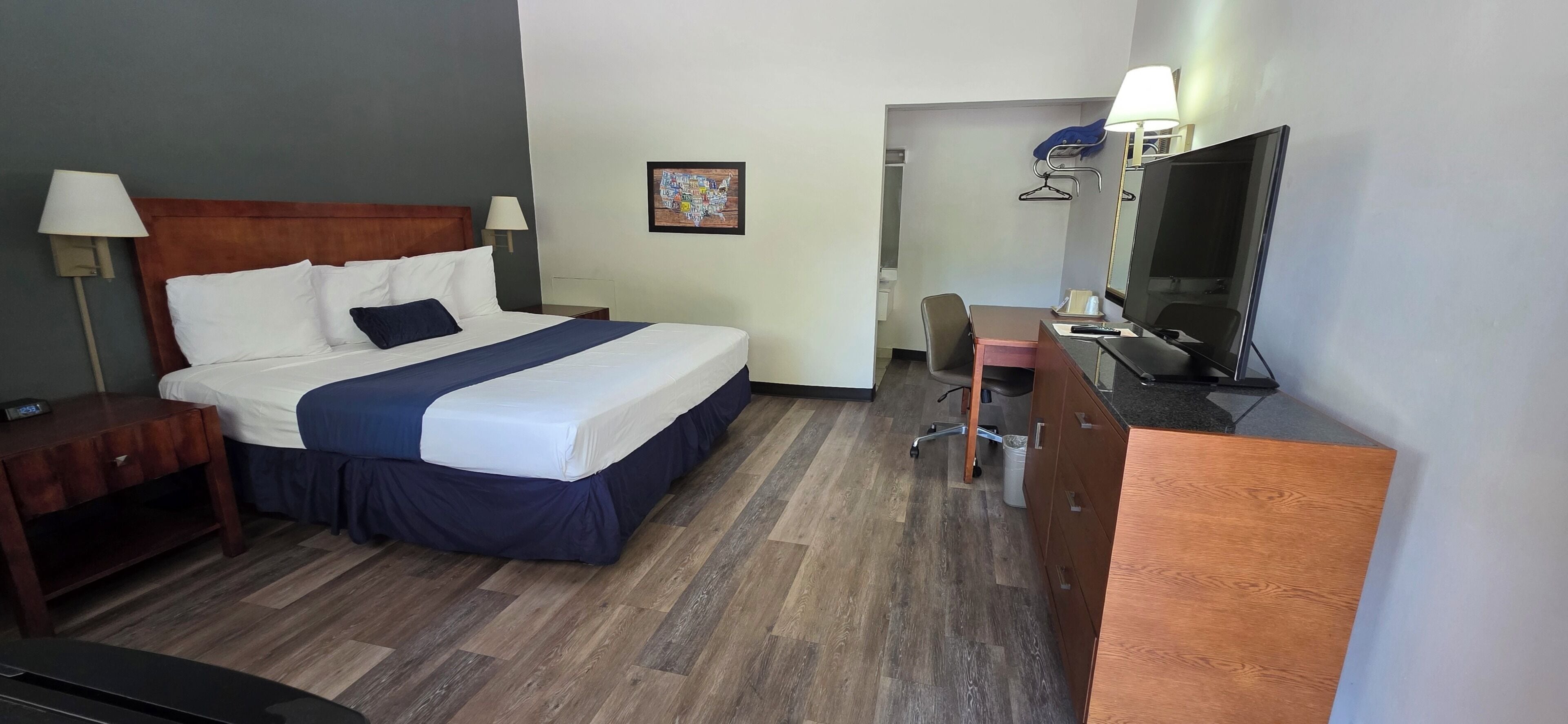 Quarto de hotel com uma cama, mesas de cabeceira, uma escrivaninha com cadeira, televisão e espelho.