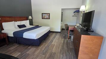 Quarto de hotel com uma cama, mesas de cabeceira, uma escrivaninha com cadeira, televisão e espelho.