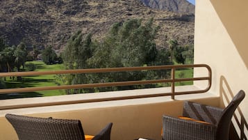 A balcony with wicker chairs and a table, overlooking a golf course and mountains.