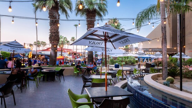 An outdoor dining area with tables and chairs, umbrellas, and palm trees. - Hyatt Palm Springs (Palm Springs)