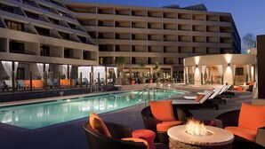 A hotel pool area with lounge chairs, a fire pit, and a large building in the background. - Hyatt Palm Springs (Palm Springs)
