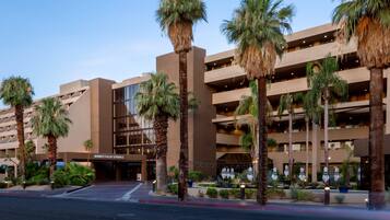 A multi-story hotel with a modern design, featuring a prominent entrance and palm trees.