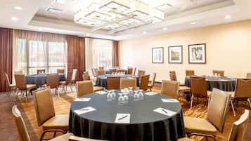 A conference room with round tables, chairs, and a large window with curtains.