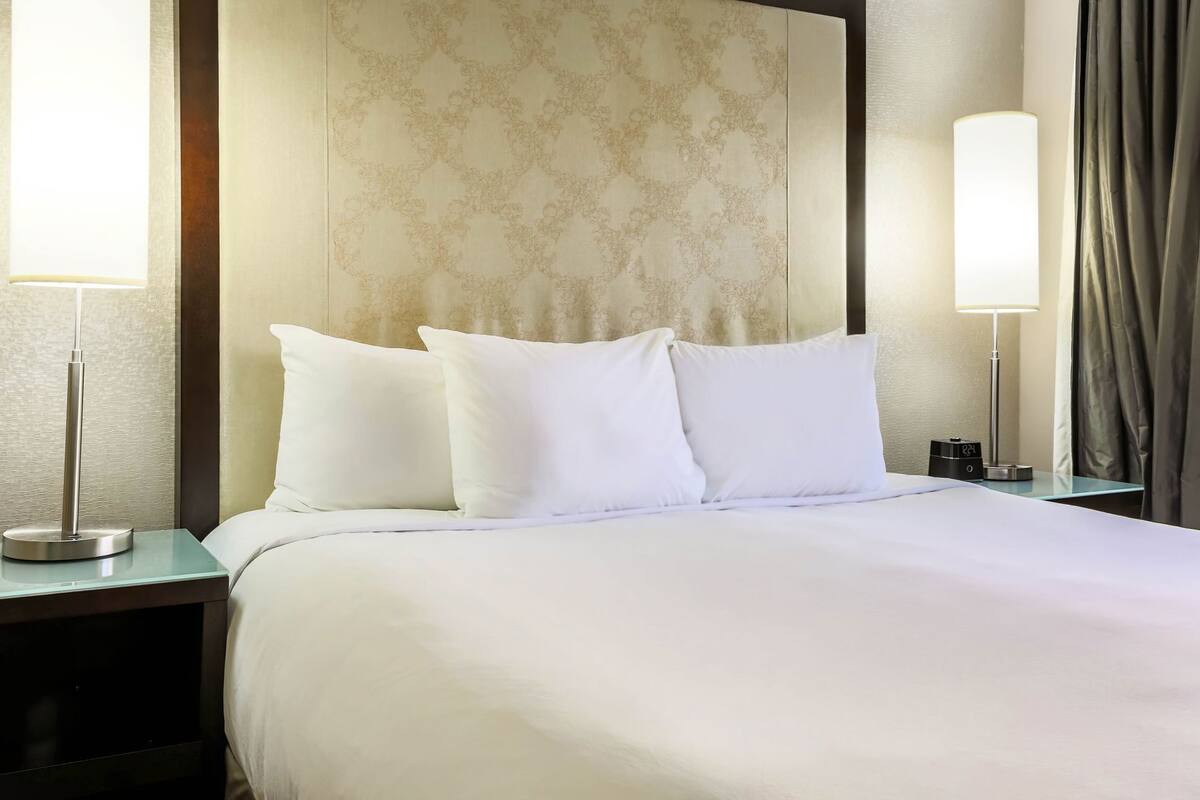 A hotel room with a large bed, two bedside lamps, a nightstand, and a wall clock.