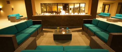 A lounge area with teal sofas, a central coffee table, and a bar with a fire feature.