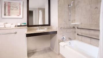 A bathroom with a bathtub, a sink, and a shower. There are handrails and a mirror above the sink.
