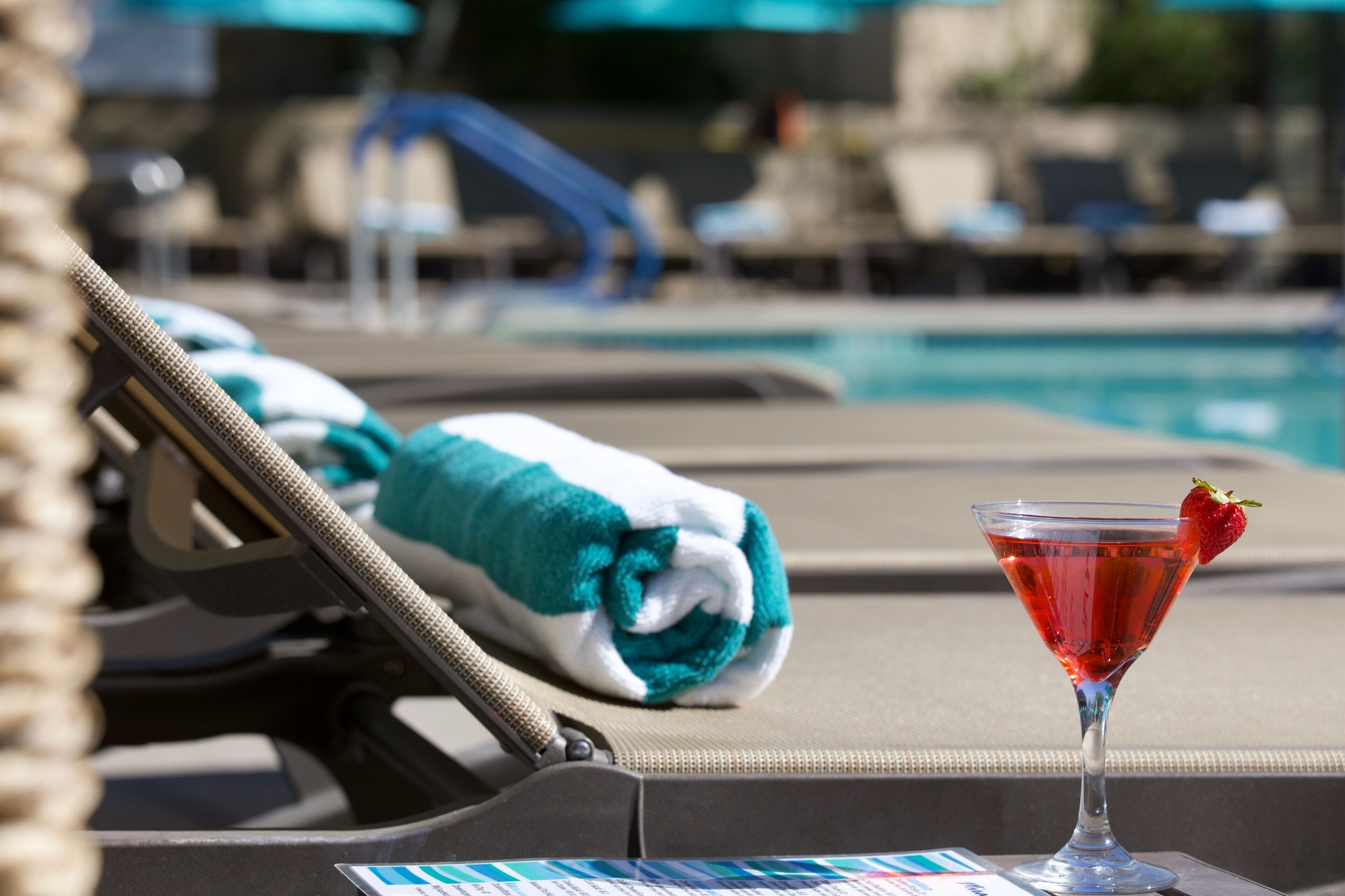 Ein Poolbereich mit Liegestuhl, zusammengelegtem Handtuch und Martini-Glas mit Erdbeere.