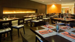 A restaurant with tables set for dining, a wall-mounted fire feature, and a modern interior design. - Hyatt Palm Springs (Palm Springs)