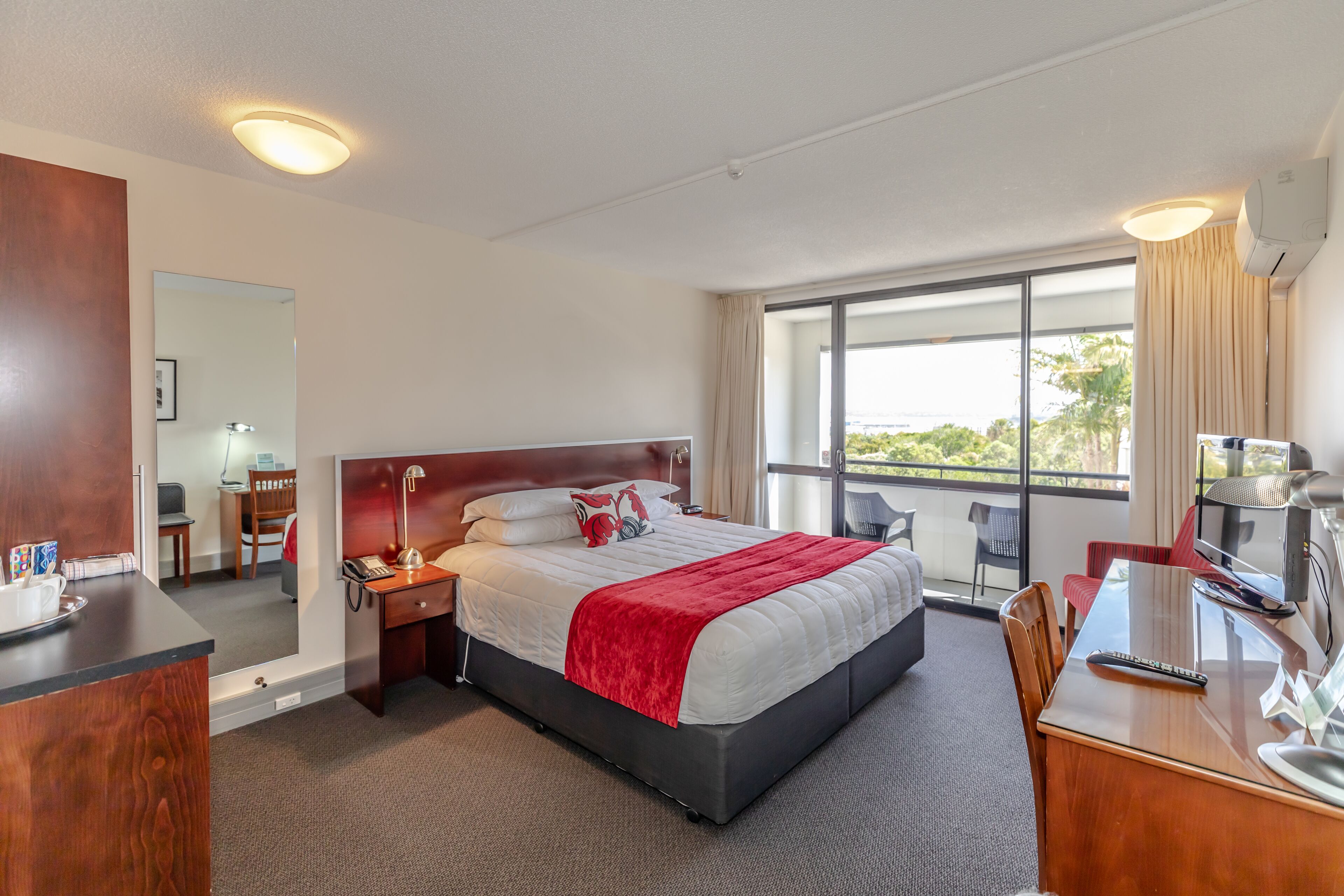 A hotel room with a large bed, a desk with a computer, a chair, and a TV.