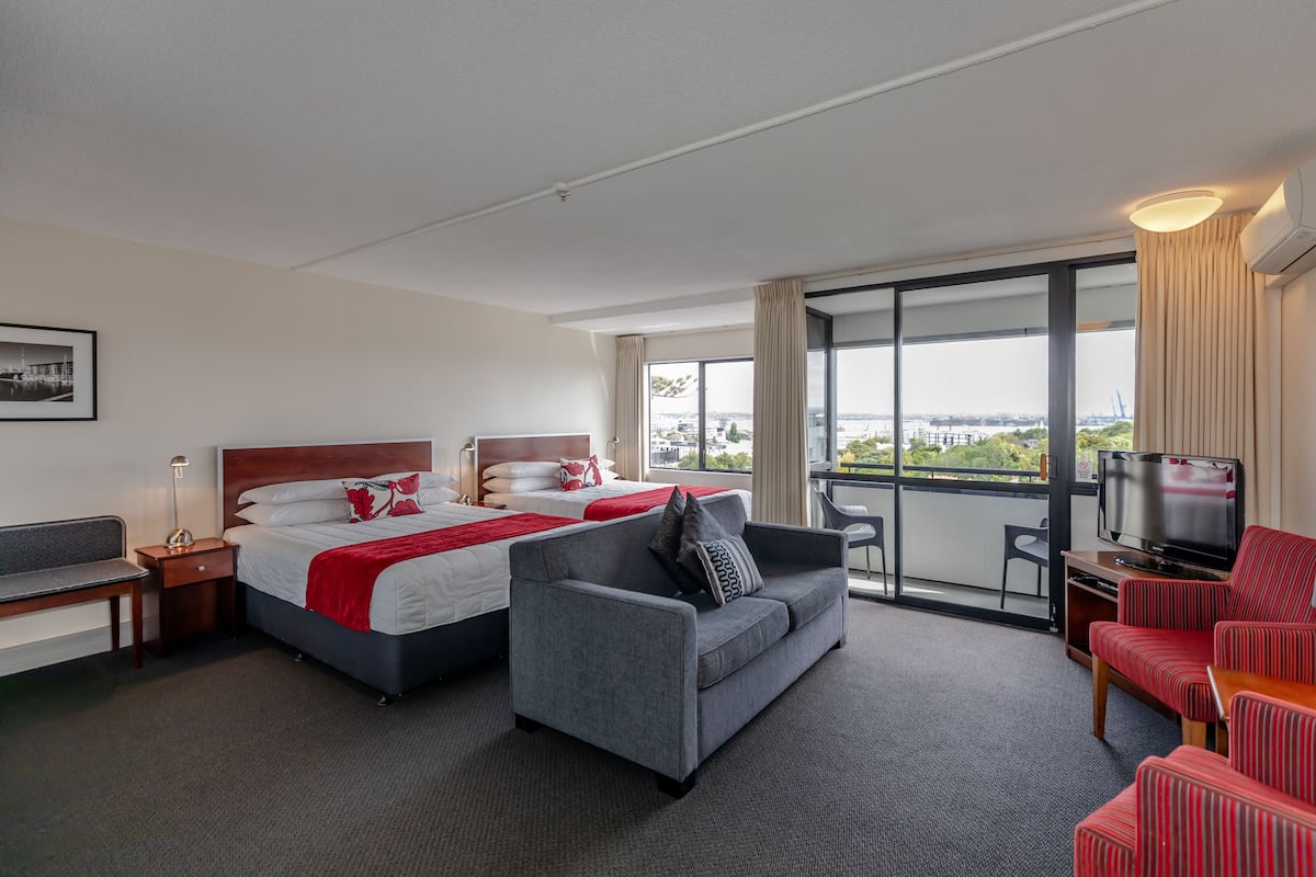 A hotel room with a large bed, a sofa, a TV, and a balcony with a city view.