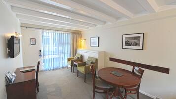 A hotel room with a wooden desk, two armchairs, a dining table, and a television on the wall.