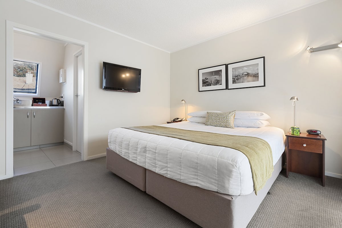 A hotel room with a bed, bedside table, lamp, and a TV on the wall.