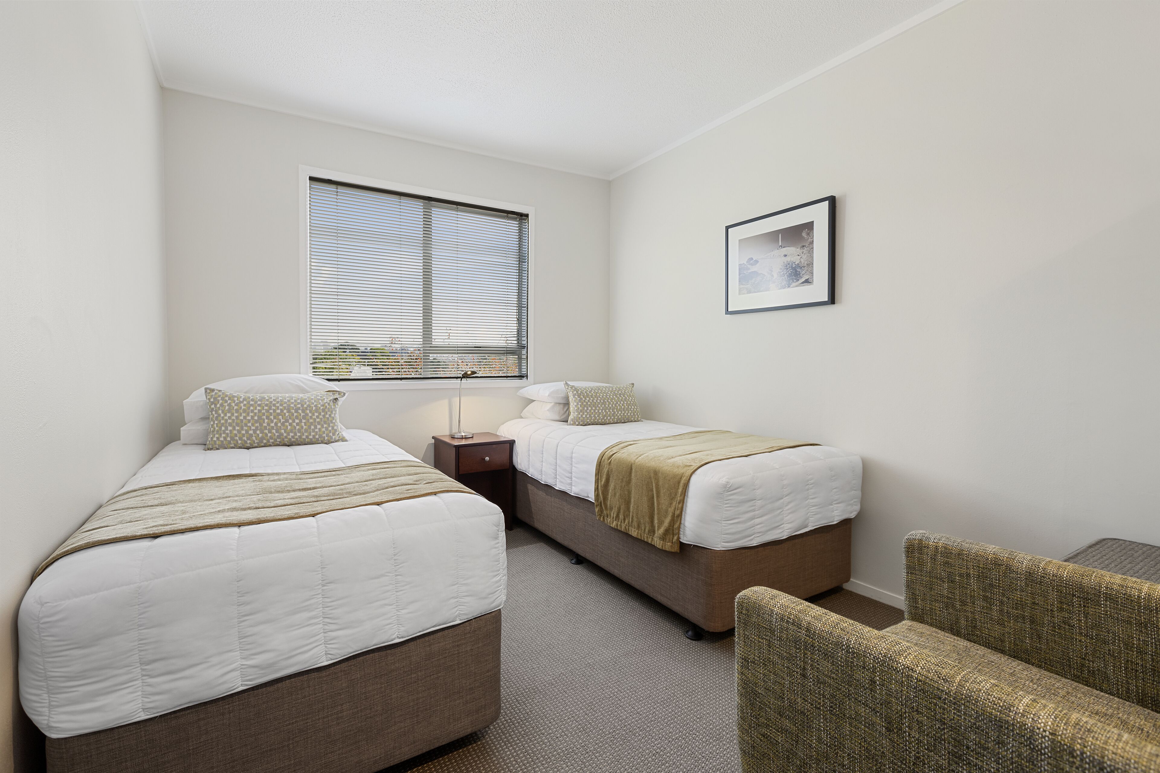 A hotel room with two beds, a window, a framed picture, and a small table.