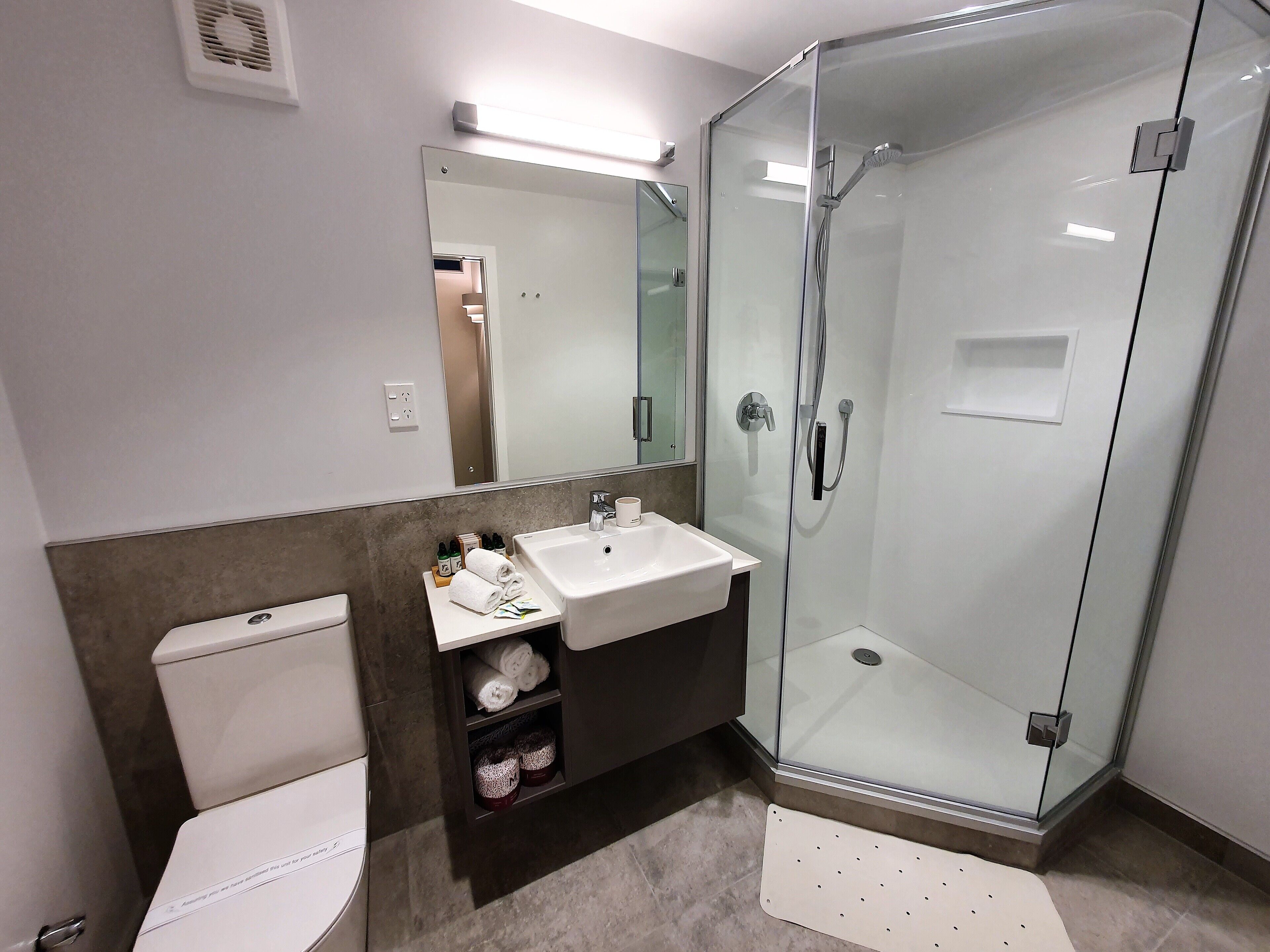 Un baño moderno con ducha envuelta en vidrio, un lavamanos blanco y un inodoro.