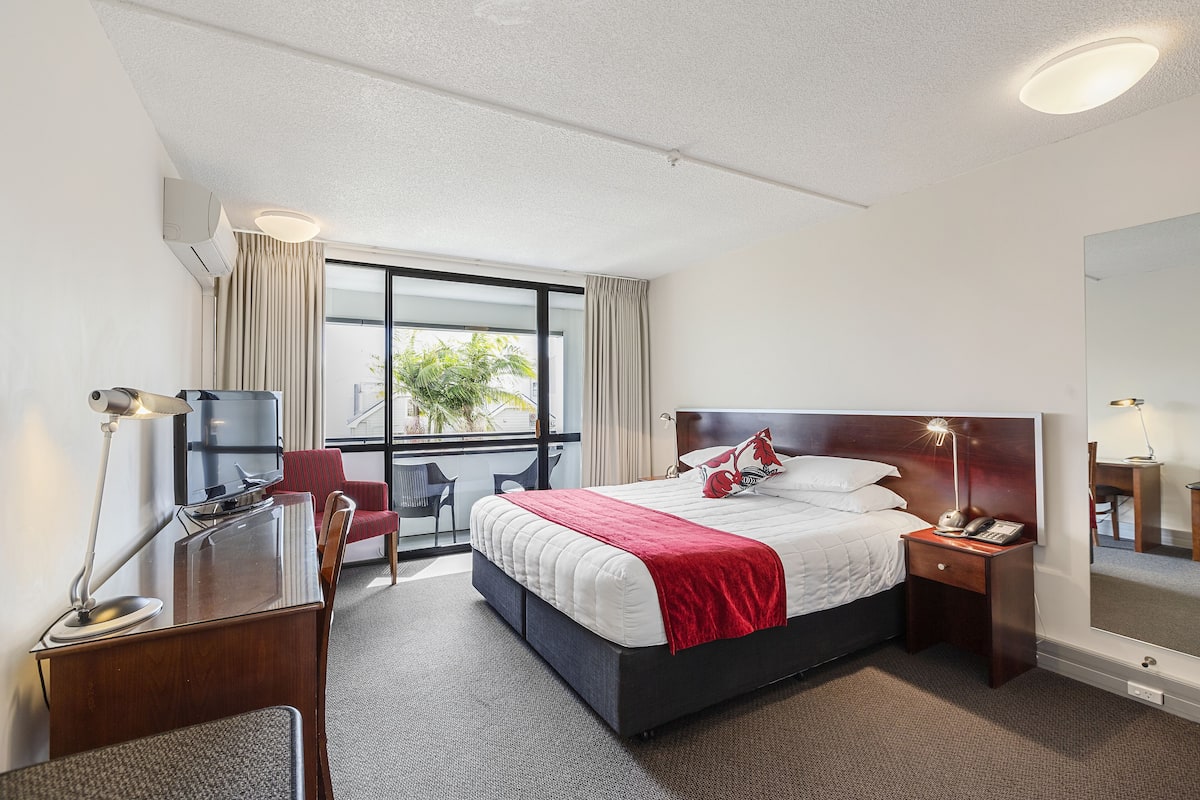 A hotel room with a bed, desk, chair, and a large window.