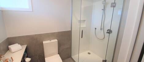 Un baño moderno con ducha de vidrio, inodoro y lavamanos con artículos de tocador.